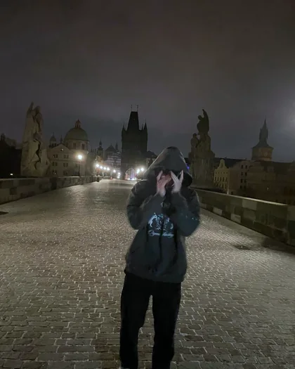 Night on Charles Bridge in Prague, a figure in a hoodie with hands at the face